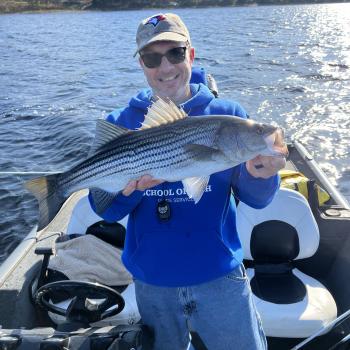 ryan holding a striped bass in front of the water